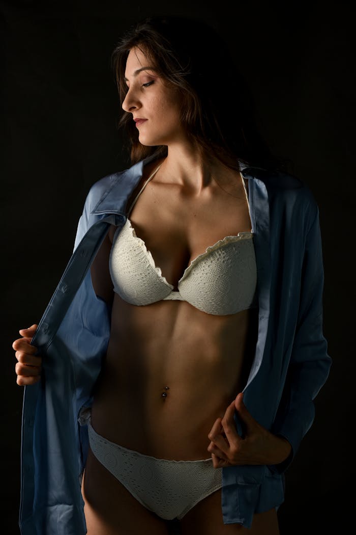 Model in lingerie posing confidently with soft lighting and shadow contrasts.